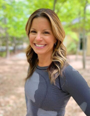A woman in grey shirt standing next to trees.