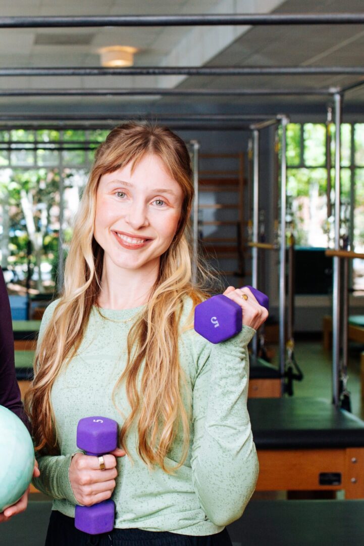 Woman exercising with purple dumbbells in a gym.