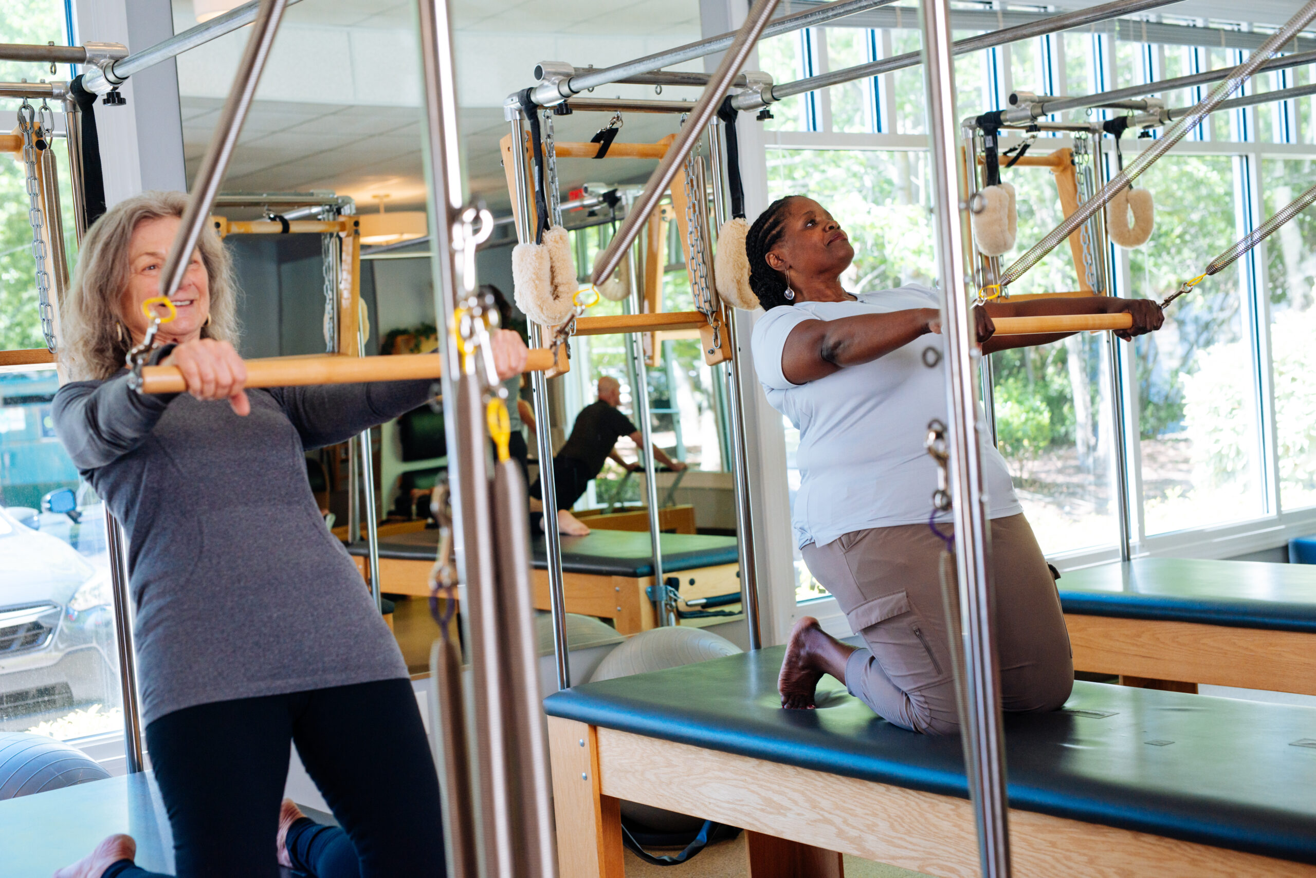 Pilates clients kneel on the Pilates Cadillac and lean back while holding the bar.