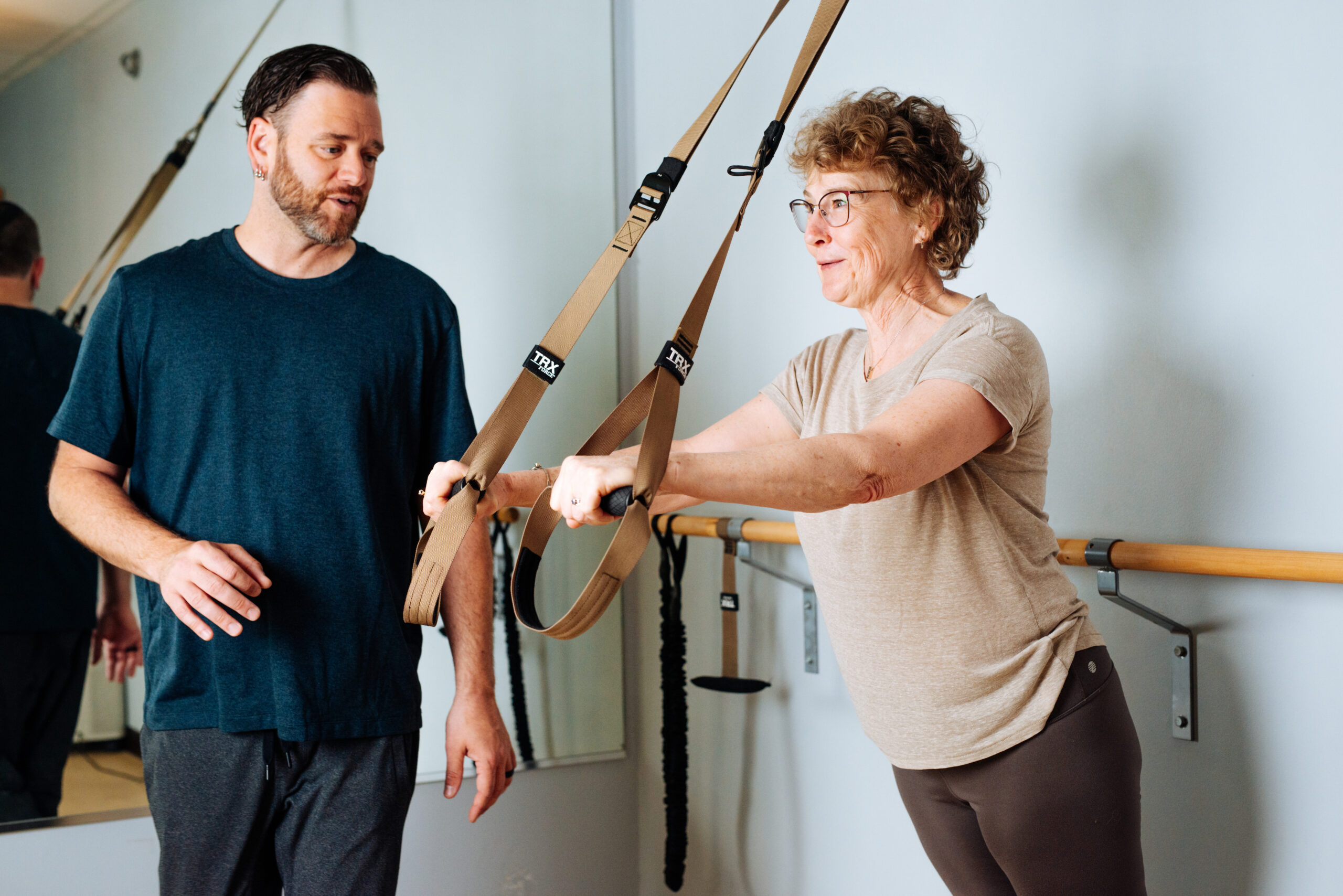 Adam works with a client on the TRX machine. She is an older woman.