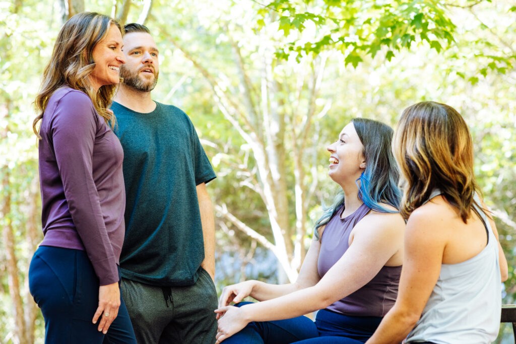 Mischa, Adam, Megan and Ashley chat outside of InsideOut Body Therapies. They are laughing and smiling while in community.