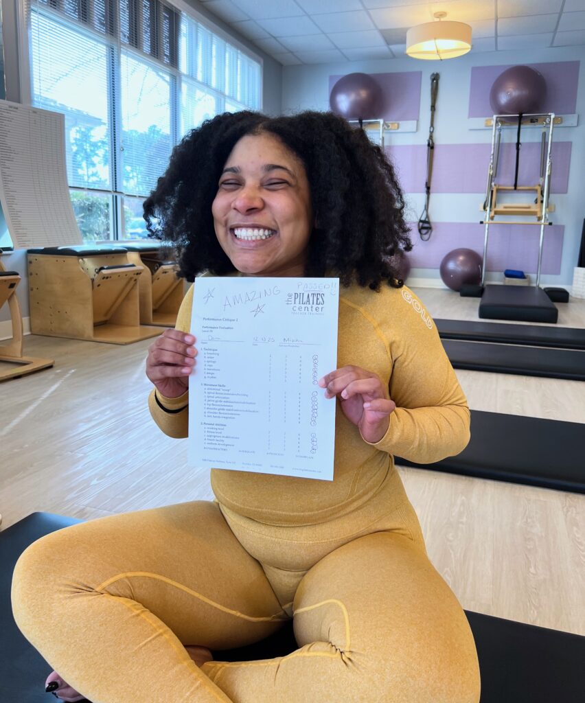 Dana smiles while holding her Pilates Teacher training assessment. She passed! Dana smiles while holding her Pilates Teacher training assessment. She passed!